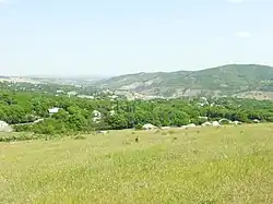 A field overlooks a hill and a valley full of trees. There are houses sporadically placed throughout the valley.