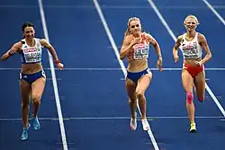 Photo of three athletes seen from the front while running on a blue athletics track