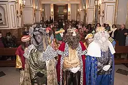 Three men disguised as kings followed by a retinue in a hall.