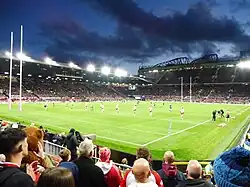 Football stadium lit up by floodlights with rugby league players and goalposts on the pitch.