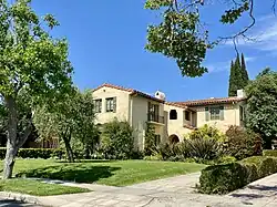 Color photograph of a California Spanish-colonial-revival-style single-family home with terra cotta roof tiles and green shutters