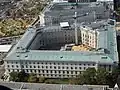 Aerial view looking west (Capitol at right / north, out of view) of the Cannon House Office Building in 2015 while undergoing latest renovation (scaffold crane in center courtyard). Longworth House Office Building adjacent and further west at top of photo. Rayburn House Office Building barely seen at photo top to the far west.