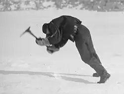 a man in polar gear leans into the face of high winds while attempting to swing an ice axe