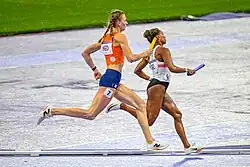 Photo of two running athletes holding batons seen from the side