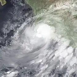 A photograph of a hurricane very close to the Pacific coast of Mexico. Its convection is fragmented and lopsided, hinting that it is about to drastically weaken.