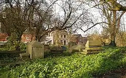 A view of the Jewish cemetery, Beth Haim, showing a various tombs among trees, with buildings in the background.