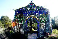 a small house-like structure made of multicolored bottles