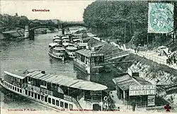 A black and white photograph of a quayside, showing several boats with passengers boarding and disembarking.