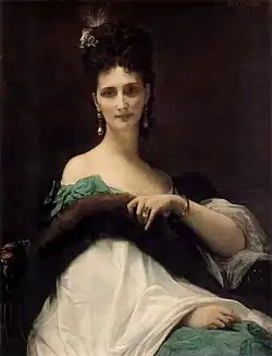 A seated woman faces forward in an elegant pose. She wears pearl earrings, a ring on her left hand, and an ornate gown with a dark fur-like stole over her shoulders. Her luminous skin contrasts with the rich fabrics.