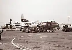 A black-and-white photograph of a twin-engine aircraft at an airport