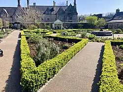 A picture of the Physic Garden, featuring paths and box hedges, with the old Grammar School in the background.