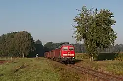 A red train crosses a field