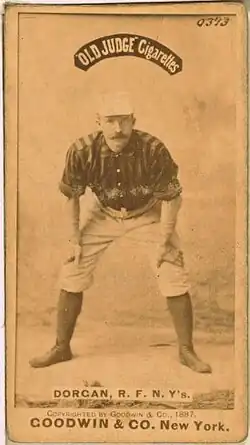 A baseball player standing facing the camera with his hands resting on his knees