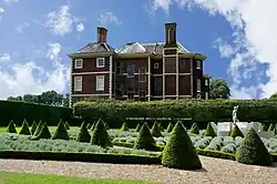A photograph of the east side of the house taken from the Cherry Garden, which is notable for its formally-landscaped pattern including conical firs
