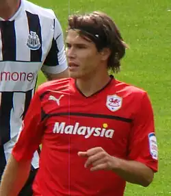 A young footballer, with long hair and in a red jersey, standing in front of his opponent during a football match between Cardiff City and Newcastle United.