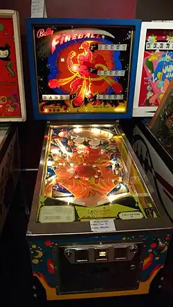 The pinball table is lit up and operational, with backglass art of a humanoid being throwing fireballs towards the viewer.