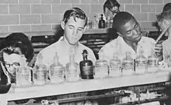 Students in a laboratory standing in front of a counter with bottles on it