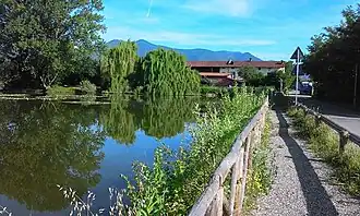 The side of a body of water with trees and a house in the background and a path to the side.
