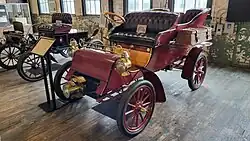 A red-colored, old-fashioned car with four seats and brass fittings