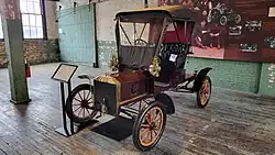 A red-colored, old-fashioned car with two seats and brass fittings