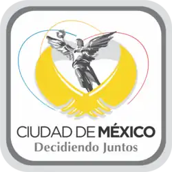 The logo features a black-and-white depiction of El Ángel, a classical-style sculpture symbolizing victory. The figure is a bare-chested angel wearing a long skirt, holding a laurel wreath in her right hand. Beneath the sculpture are two stylized golden wings. The text "Ciudad de México" appears below in uppercase black letters, with "México" in bold. Underneath is the slogan "Decidiendo Juntos", following the same font pattern. The entire composition is enclosed within a gray squircle.