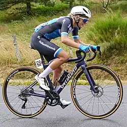 Eline Jansen riding a bicycle on pavement, wearing a black and blue jersey