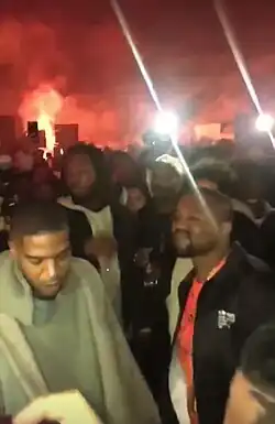 The two members of Kids See Ghosts stood in front of a bonfire