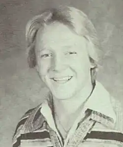 A white teenager with blond hair is wearing layered collared shirts and smiling into the camera.