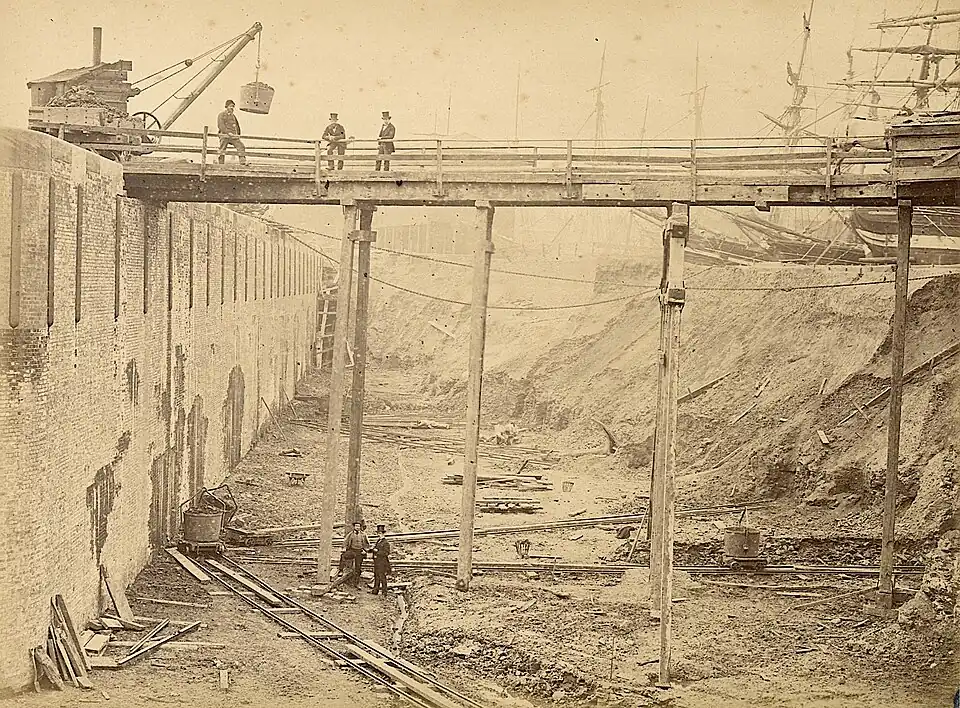 Enlargement (top-hatted directors posing, early 1867). Note sailing ships — held back by temporary earth dam.