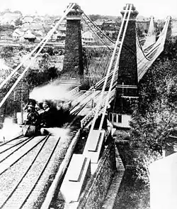 Three railway lines merge into one, crossing a bridge. A train engine has crossed the bridge and is moving into the left-most line.