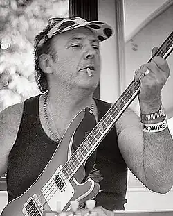 A close-up of a man smoking a cigarette and playing a bass guitar