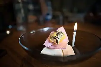 Two pieces of meringue of different colors, one on top of the other, accompanied by a golden foil, and decorated with a candle.