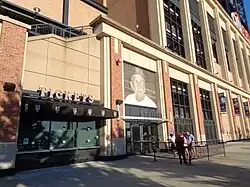 Exterior of a stadium. The admission gate has a large picture of Stengel in a Mets cap over it.