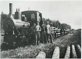 A monochrome photograph of a steam locomotive hauling logs, and its crew