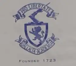 A hand drawing of the Original Wallace Hall (Thornhill) crest. It contains a blue shield with a lion contained inside. An arm with a blade sticks out the top of the shield. The shield has two banners below and above it, enscribed with Latin, reading above: "PRO-LIBERTATE" and below: "UALLACIA-ACADEMIA"