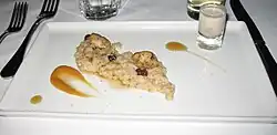 Two oysters and a handful of raisins rest atop a line of oatmeal. On either side is a streak of maple syrup. The dish is served on a white tray.