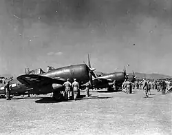 A black and white photograph of 3 fighter aircraft docked at a base while soldiers and officers move around them