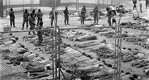 Prisoners lie on the ground as they are watched over by masked soldiers with weapons