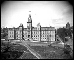 A black and white photograph of the Providence Hospital building, featuring a tall clock tower capped by a cross