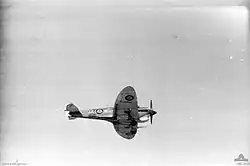 A black and white photograph of an aircraft with military style painting flying.