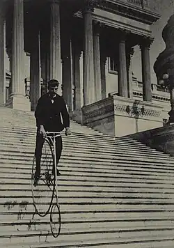 A photo of a man on a penny-farthing bicycle descending the steps of the US Capitol Building