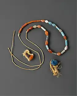 A necklace of different shaped and sized stones; a biconical bead of carnelian on a frayed loop; a blue scarab on frayed loop