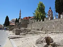 A ruined medieval wall, in front of a mosque and other modern buildings