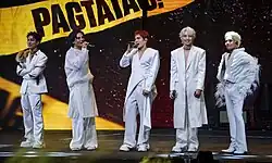 A group photo of SB19 onstage, each with a handheld microphone