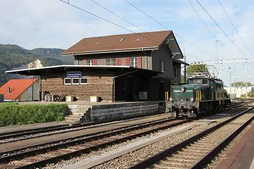Green locomotive in front of two-story building with gabled roof