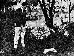 A black-and-white image of a young man standing over a reclining woman