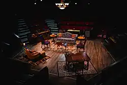 A fisheye photo of a small in-the-round stage with blocks of four or five rows of seats on each side and a partially full audience.