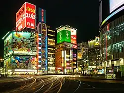 Brightly lit and colorful buildings at night in Tokyo, with automobile light trails in the foreground.