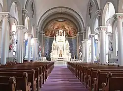 Looking down central aisle with pews on either side; line of pillars connected at tops by arches on either side; altar under half-dome at far end