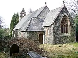 A small stone church seen from the southeast with a short chancel, a porch at the southeast, a buttressed nave, and a west bellcote